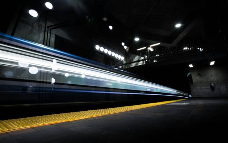 A fast-moving train captured with light trails in a dark underground station with a yellow safety strip.